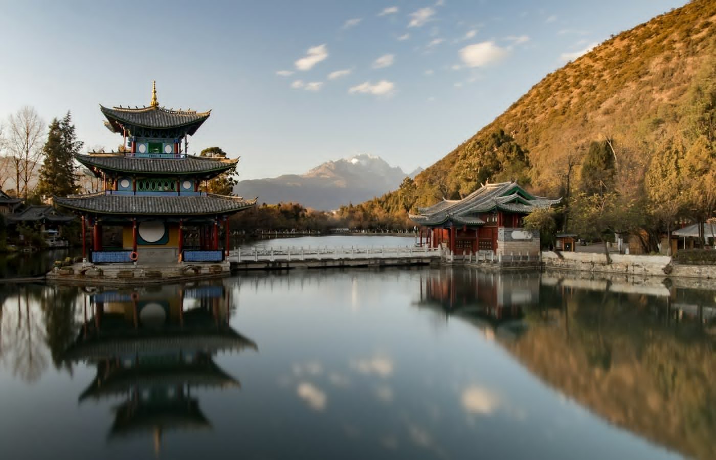 A pavilion and stone bridge reflected in still water, with mountains behind